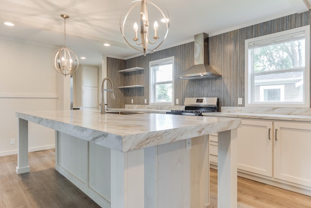 kitchen with pendant lighting, sink, stainless steel stove, wall chimney exhaust hood, and an island with sink