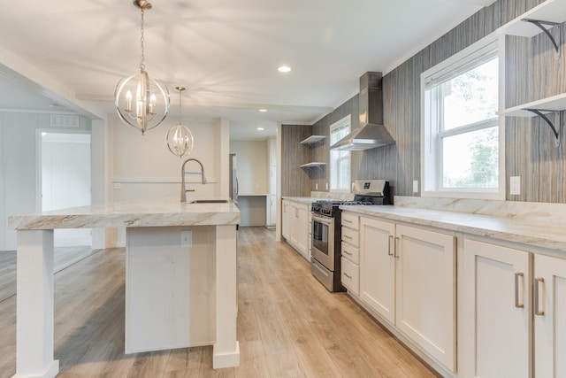 kitchen with sink, wall chimney range hood, decorative light fixtures, light hardwood / wood-style floors, and stainless steel range with gas cooktop