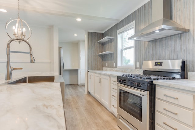 kitchen with wall chimney range hood, light hardwood / wood-style flooring, light stone countertops, white cabinetry, and stainless steel range with gas stovetop