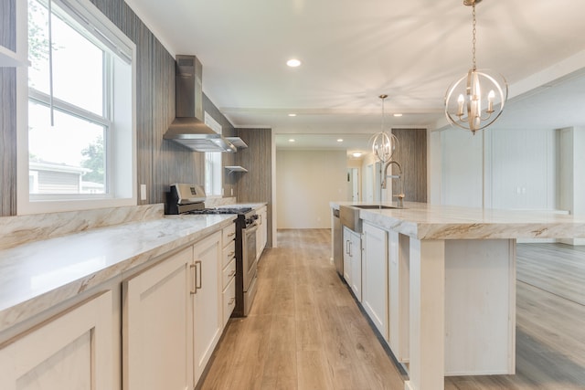 kitchen featuring sink, hanging light fixtures, wall chimney range hood, a kitchen island with sink, and appliances with stainless steel finishes