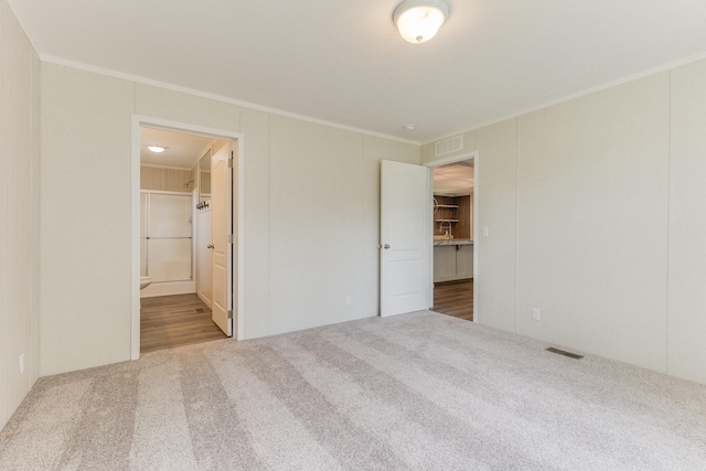 unfurnished bedroom with carpet floors, ornamental molding, and ensuite bath