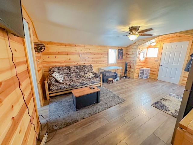 living room with ceiling fan, wood walls, wood-type flooring, and lofted ceiling