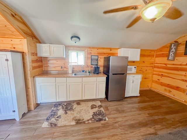 kitchen featuring stainless steel fridge, sink, light hardwood / wood-style flooring, white cabinetry, and wood walls