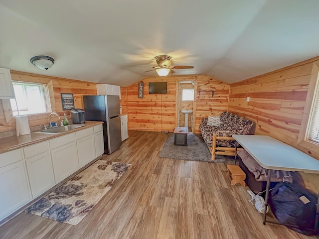 interior space with wood walls, sink, vaulted ceiling, light hardwood / wood-style floors, and stainless steel refrigerator