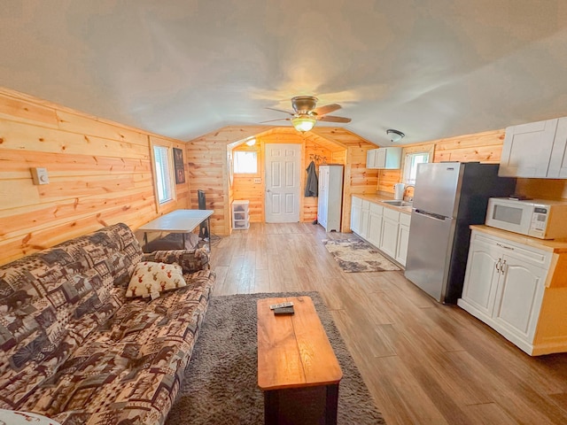 living room featuring light wood-type flooring, ceiling fan, wooden walls, sink, and lofted ceiling