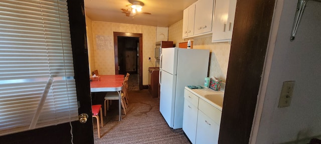 kitchen with dark colored carpet, ceiling fan, white fridge, and white cabinetry