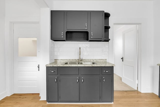 kitchen with sink, light stone counters, light hardwood / wood-style floors, gray cabinets, and decorative backsplash