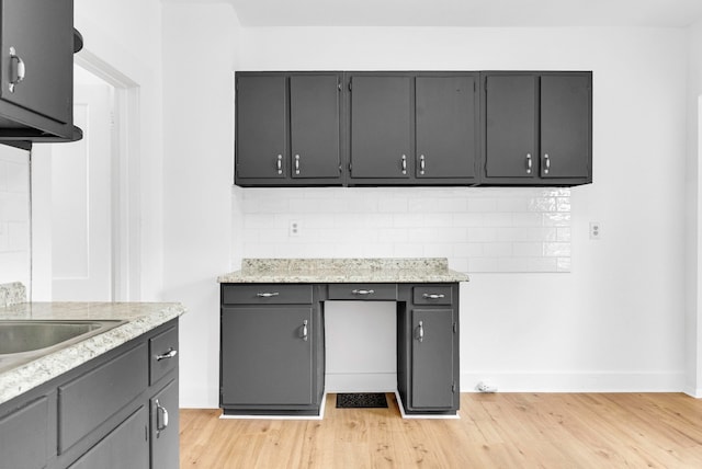 kitchen featuring sink, light stone counters, light wood-type flooring, and backsplash