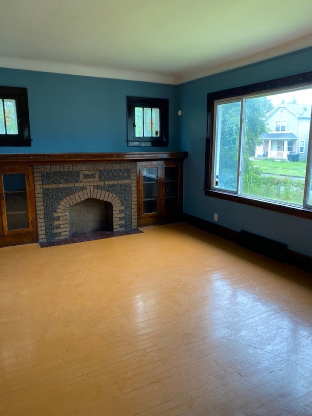 unfurnished living room with a wealth of natural light, light hardwood / wood-style floors, and a brick fireplace