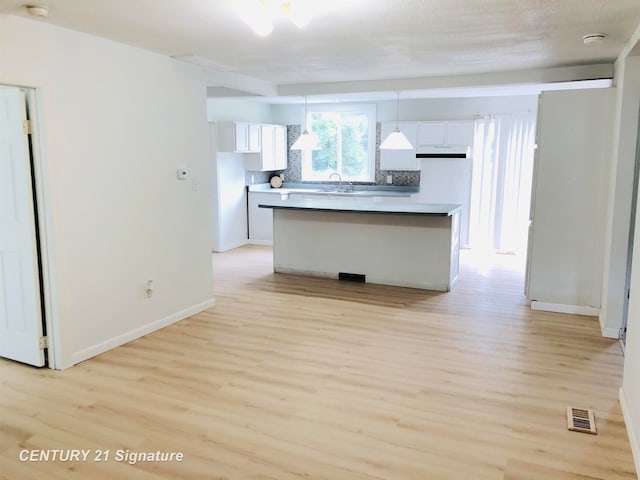 kitchen featuring pendant lighting, a center island, backsplash, white cabinets, and light hardwood / wood-style flooring