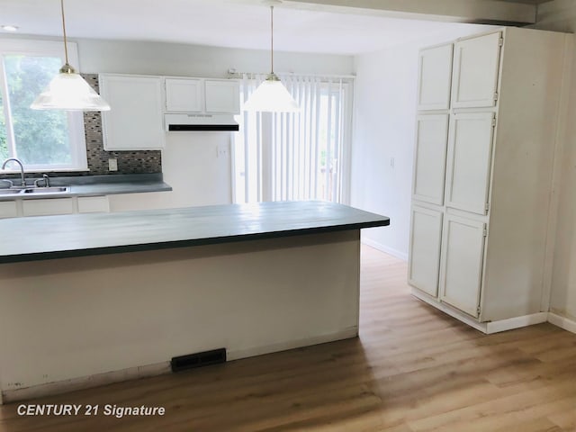 kitchen with white cabinets, light hardwood / wood-style floors, hanging light fixtures, and sink