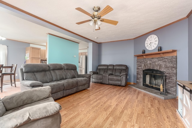 living room featuring light wood-type flooring, ornamental molding, a textured ceiling, ceiling fan, and a stone fireplace