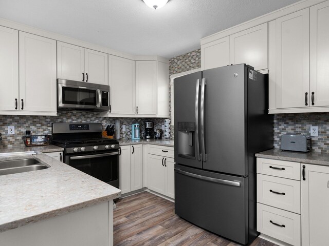 94 Charter Ct, Manistee, MI 49660 - kitchen with stainless steel appliances, tasteful backsplash, white cabinetry, a sink, and light wood-type flooring