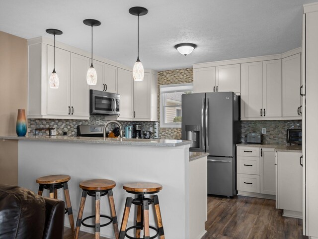 94 Charter Ct, Manistee, MI 49660 - kitchen with appliances with stainless steel finishes, a peninsula, a kitchen bar, backsplash, and white cabinets