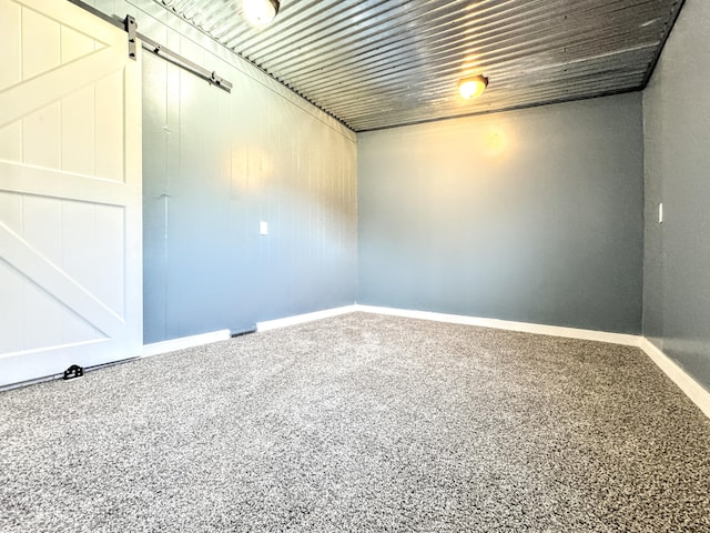 spare room featuring a barn door, baseboards, and carpet flooring