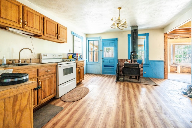 kitchen featuring light wood-type flooring, sink, pendant lighting, a wood stove, and white range with electric cooktop