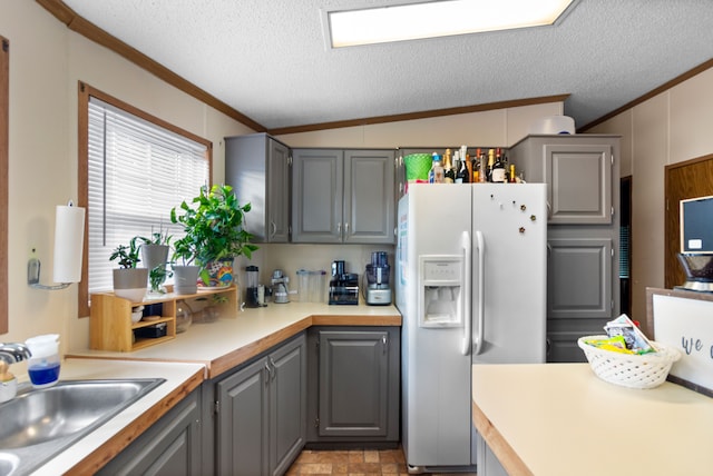 kitchen with gray cabinetry, white refrigerator with ice dispenser, crown molding, a textured ceiling, and lofted ceiling