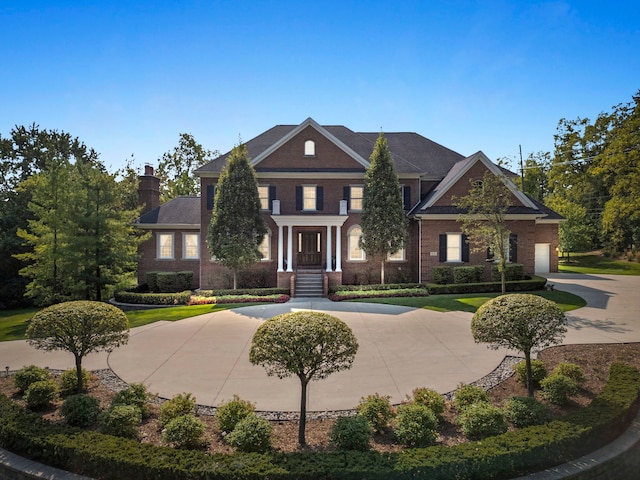 colonial inspired home featuring a chimney, curved driveway, and brick siding