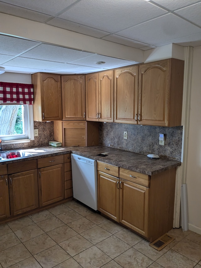 kitchen featuring dishwasher, a drop ceiling, backsplash, sink, and light tile patterned floors