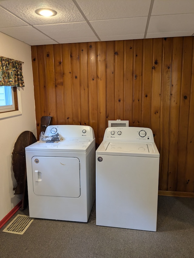 clothes washing area featuring washing machine and clothes dryer, carpet flooring, and wood walls