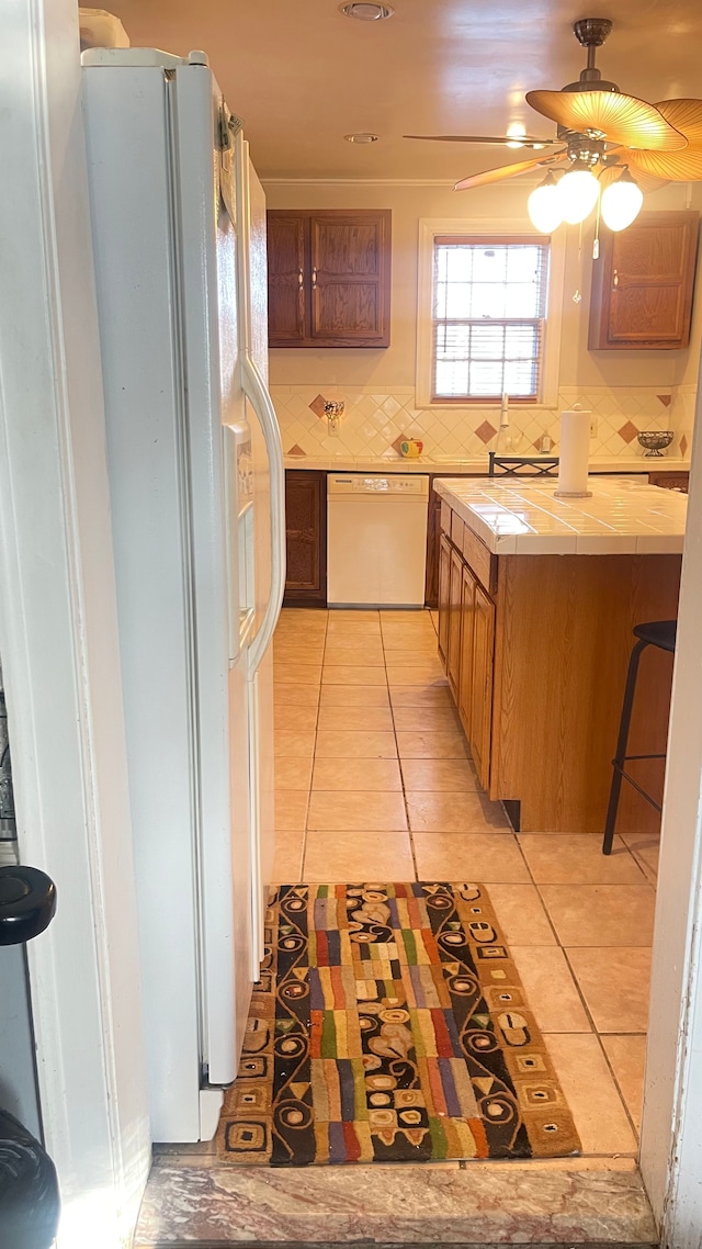 kitchen featuring light tile patterned floors, white appliances, ceiling fan, backsplash, and tile counters