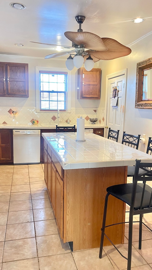 kitchen featuring light tile patterned flooring, tile countertops, backsplash, a kitchen breakfast bar, and white dishwasher