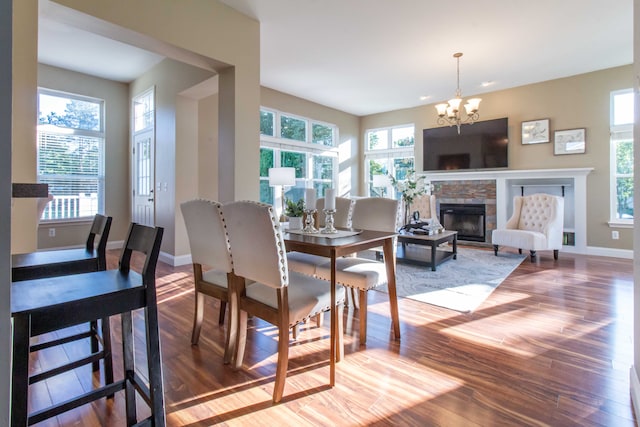 dining space featuring a stone fireplace, wood-type flooring, and an inviting chandelier