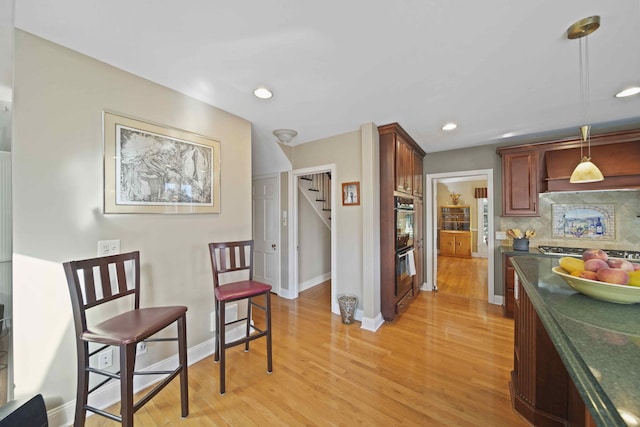 kitchen featuring backsplash, black double oven, stainless steel gas cooktop, pendant lighting, and light hardwood / wood-style flooring