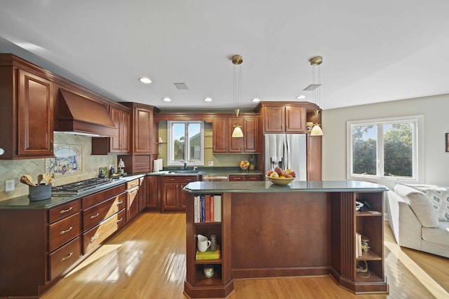 kitchen with a center island, appliances with stainless steel finishes, decorative light fixtures, light hardwood / wood-style floors, and custom range hood