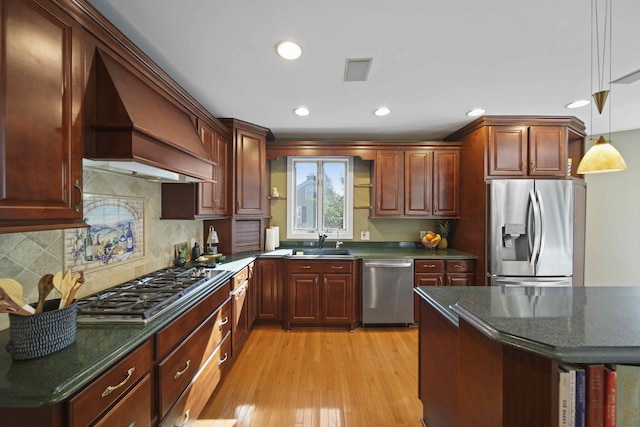 kitchen featuring hanging light fixtures, stainless steel appliances, a kitchen breakfast bar, light hardwood / wood-style floors, and custom range hood