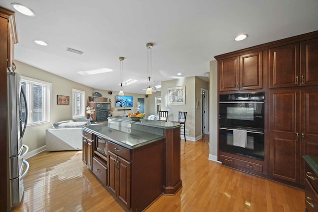 kitchen with black double oven, hanging light fixtures, stainless steel fridge, light wood-type flooring, and a kitchen island