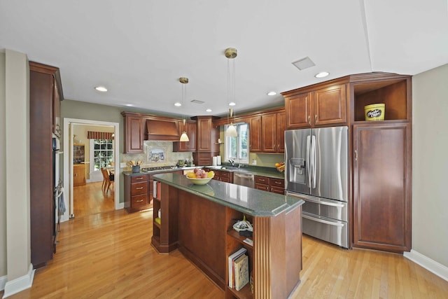 kitchen with light wood-type flooring, custom range hood, stainless steel appliances, pendant lighting, and a kitchen island