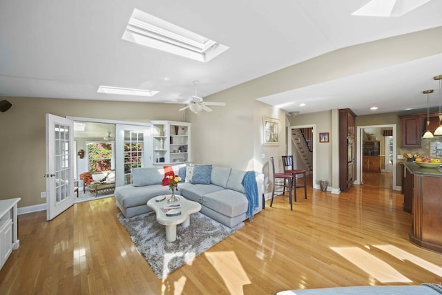 living room featuring vaulted ceiling with skylight, ceiling fan, french doors, and light hardwood / wood-style flooring