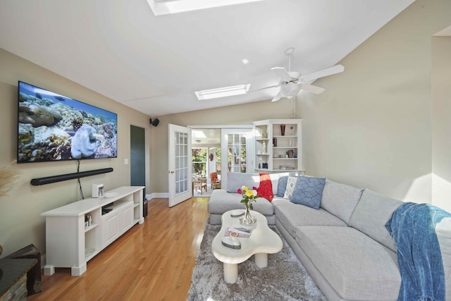 living room featuring ceiling fan, french doors, light wood-type flooring, and vaulted ceiling with skylight