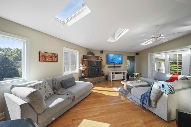 living room featuring a wood stove, a wealth of natural light, light hardwood / wood-style floors, and lofted ceiling with skylight