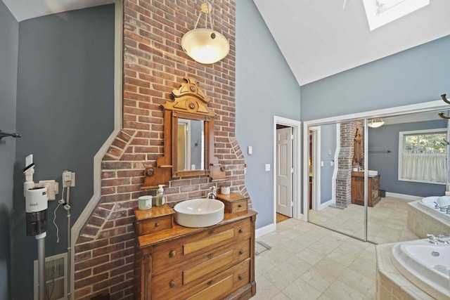 bathroom featuring a skylight, high vaulted ceiling, brick wall, tiled tub, and vanity