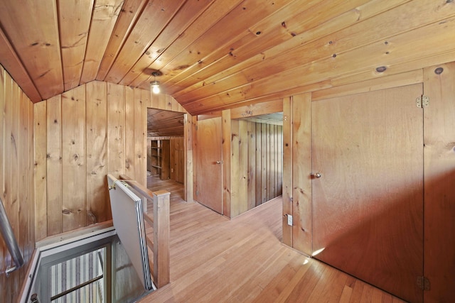 hallway featuring light wood-type flooring, wood ceiling, lofted ceiling, and wood walls