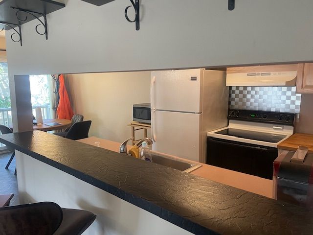 kitchen with white appliances, a kitchen breakfast bar, sink, decorative backsplash, and range hood