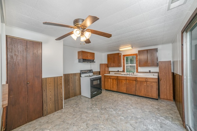 kitchen with white range with electric cooktop, sink, wooden walls, ceiling fan, and ornamental molding