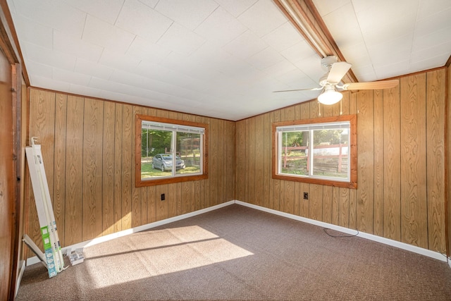 carpeted empty room with plenty of natural light, wood walls, and vaulted ceiling