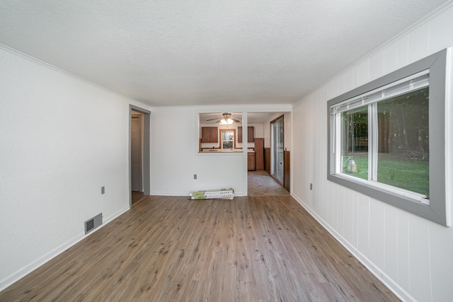 unfurnished living room featuring a textured ceiling, light hardwood / wood-style flooring, and ornamental molding