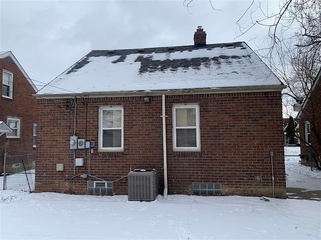 snow covered rear of property featuring central AC unit