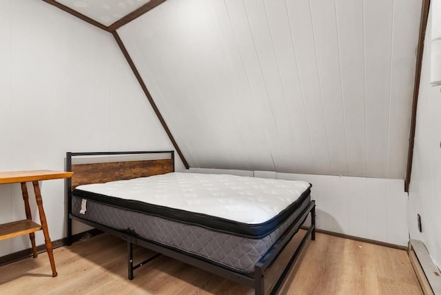 bedroom with lofted ceiling, light wood-type flooring, wooden walls, and a baseboard heating unit