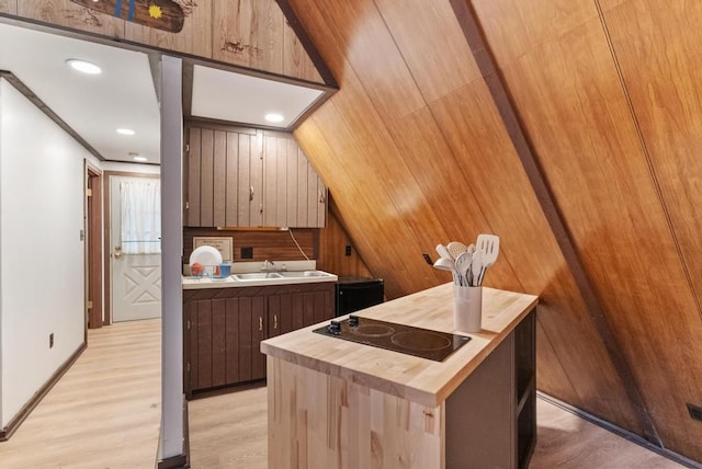 kitchen featuring light wood-type flooring, black electric cooktop, wooden walls, sink, and butcher block counters