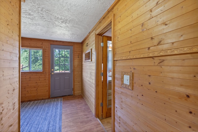 entryway featuring light wood-type flooring, a textured ceiling, and wooden walls