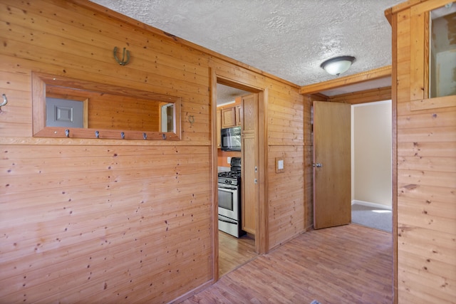 hall featuring light hardwood / wood-style floors, a textured ceiling, and wooden walls