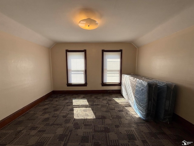 additional living space with dark colored carpet and vaulted ceiling