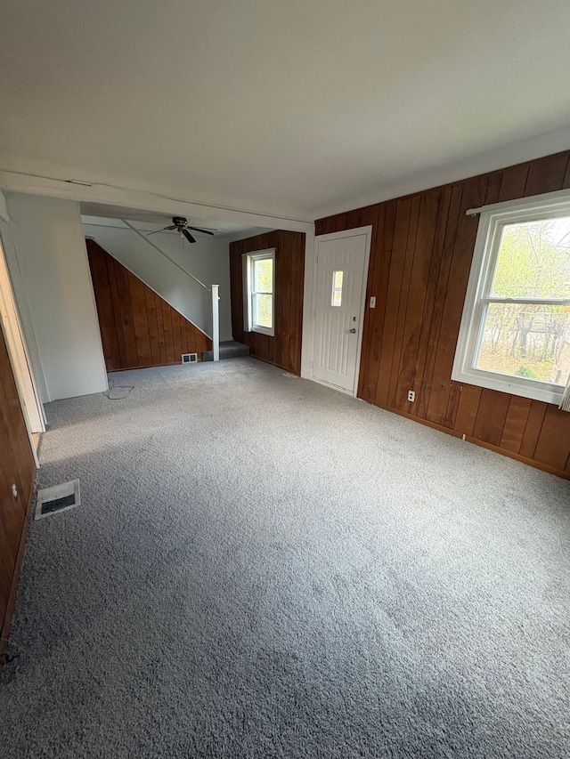 unfurnished living room featuring carpet, ceiling fan, a wealth of natural light, and wood walls