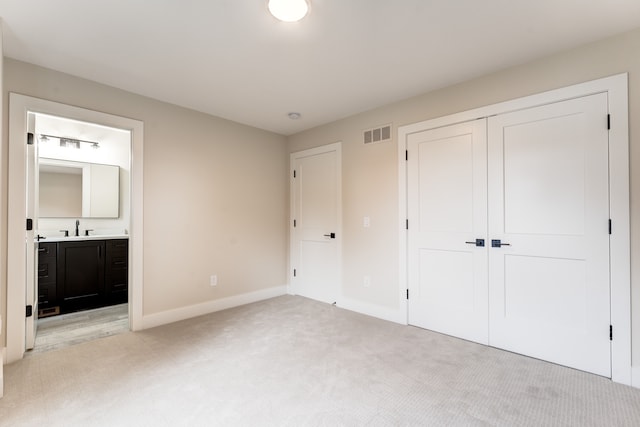 unfurnished bedroom with connected bathroom, a closet, sink, and light colored carpet