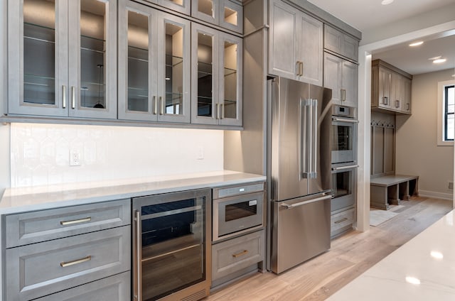 kitchen with light stone countertops, appliances with stainless steel finishes, gray cabinetry, light hardwood / wood-style floors, and wine cooler